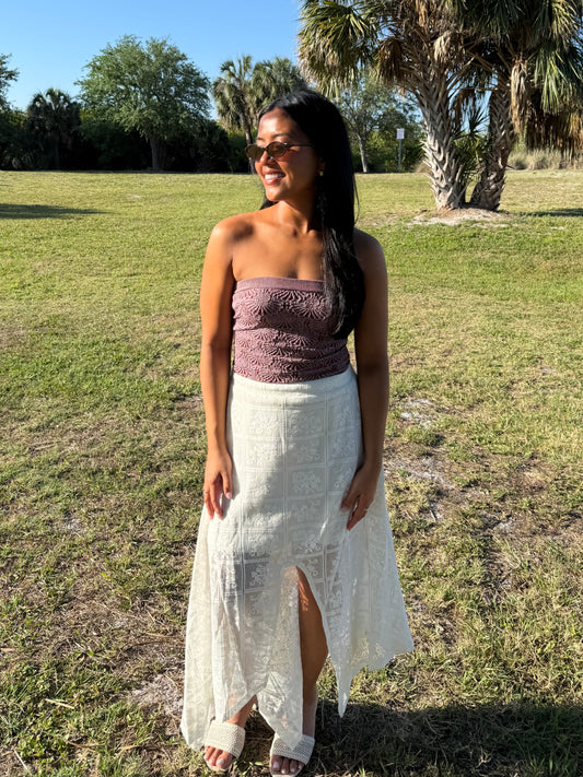 Woman wearing a strapless top and white skirt standing in a grassy field with trees in the background