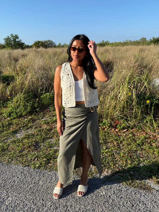 Woman standing in a field wearing a white sleeveless top, green skirt, and sunglasses.