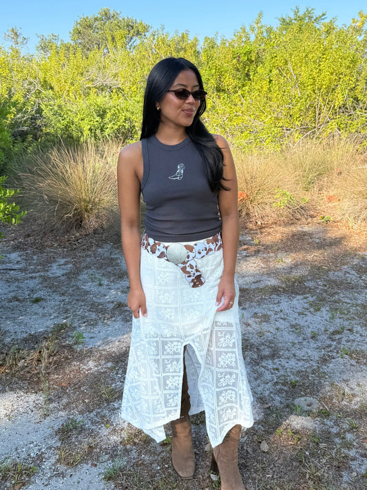 Woman standing outdoors in a natural setting wearing sunglasses, a tank top, and a long white skirt.