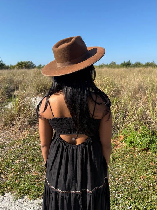 Person wearing a brown hat and black dress standing in a field with a clear blue sky.