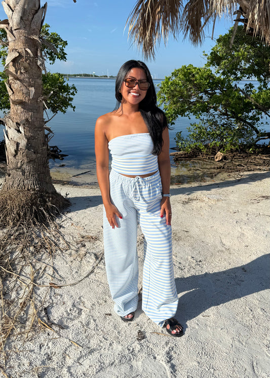 woman wearing striped top and striped pants on sand and water background