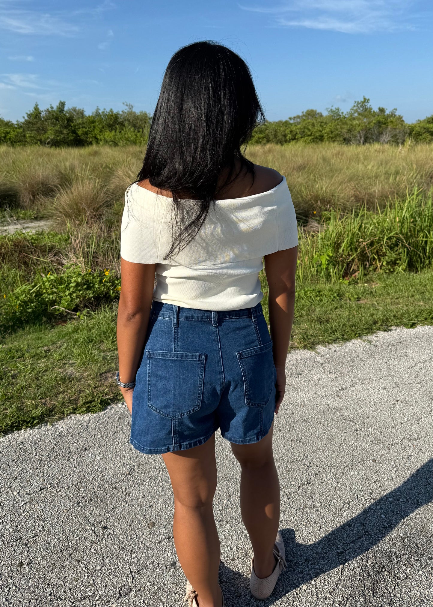 woman wearing a white top and denim shorts on a grass background
