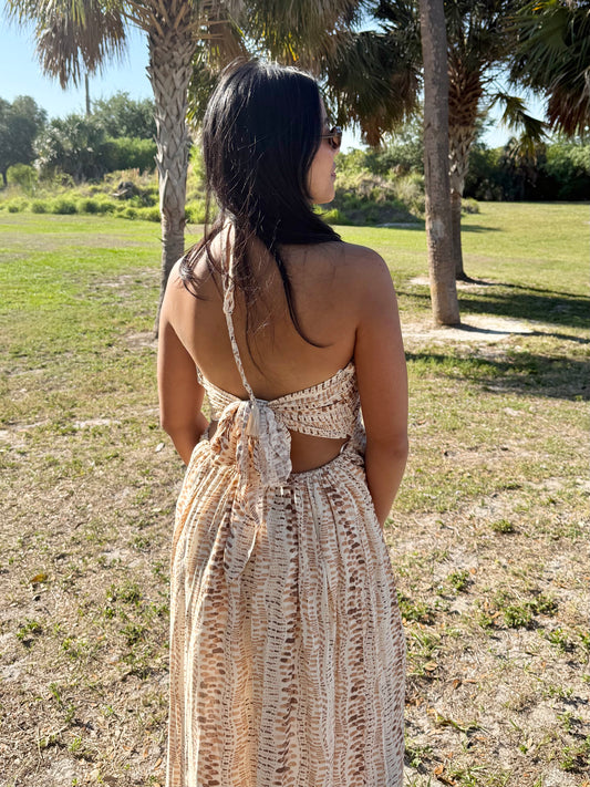 Woman in a long, open-back dress standing in a grassy area with trees.