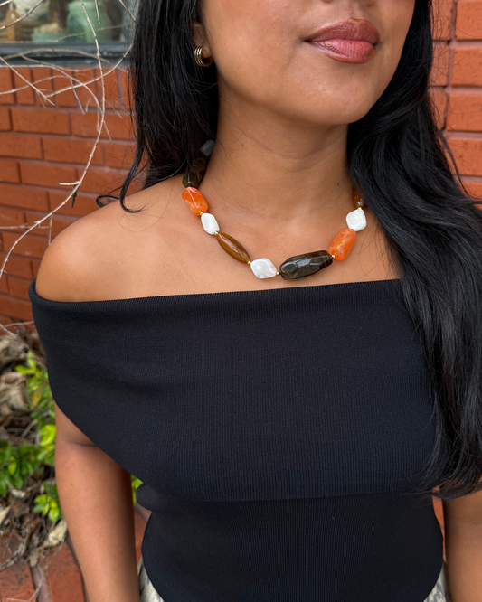 Women wearing a beaded orange, brown and white necklace with a black off the shoulder top