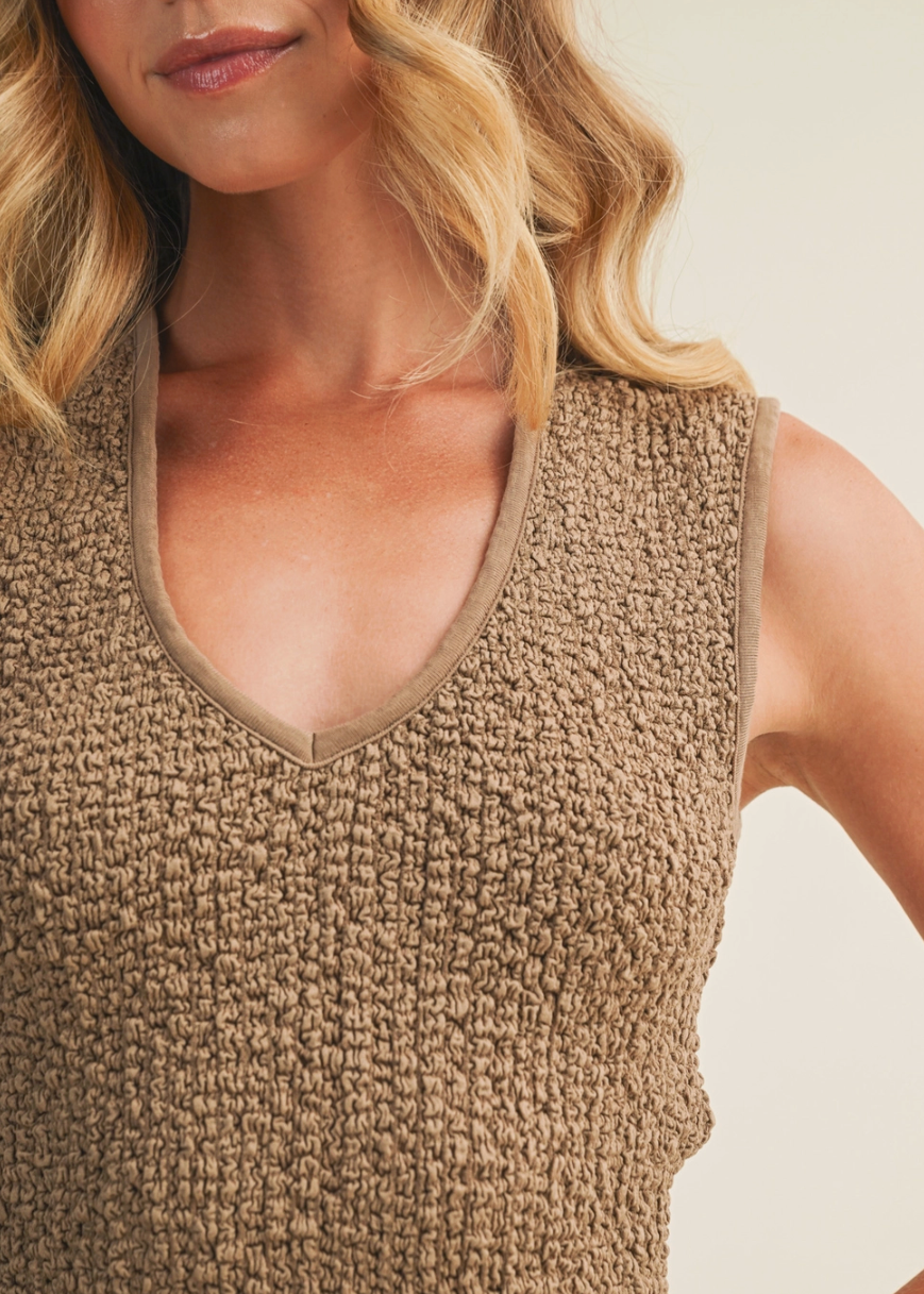 Woman wearing a textured beige sleeveless top against a neutral background