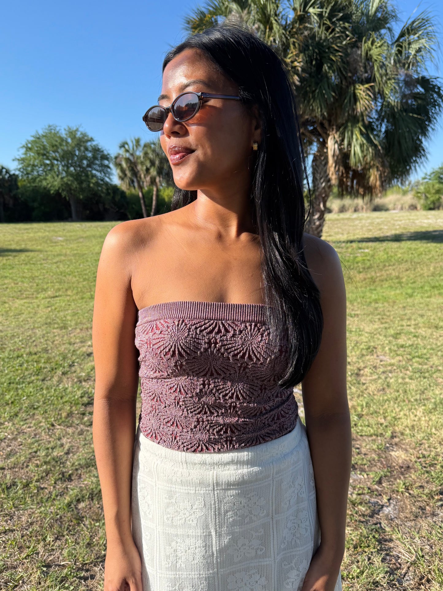 Woman wearing a strapless top and white skirt outdoors with palm trees in the background