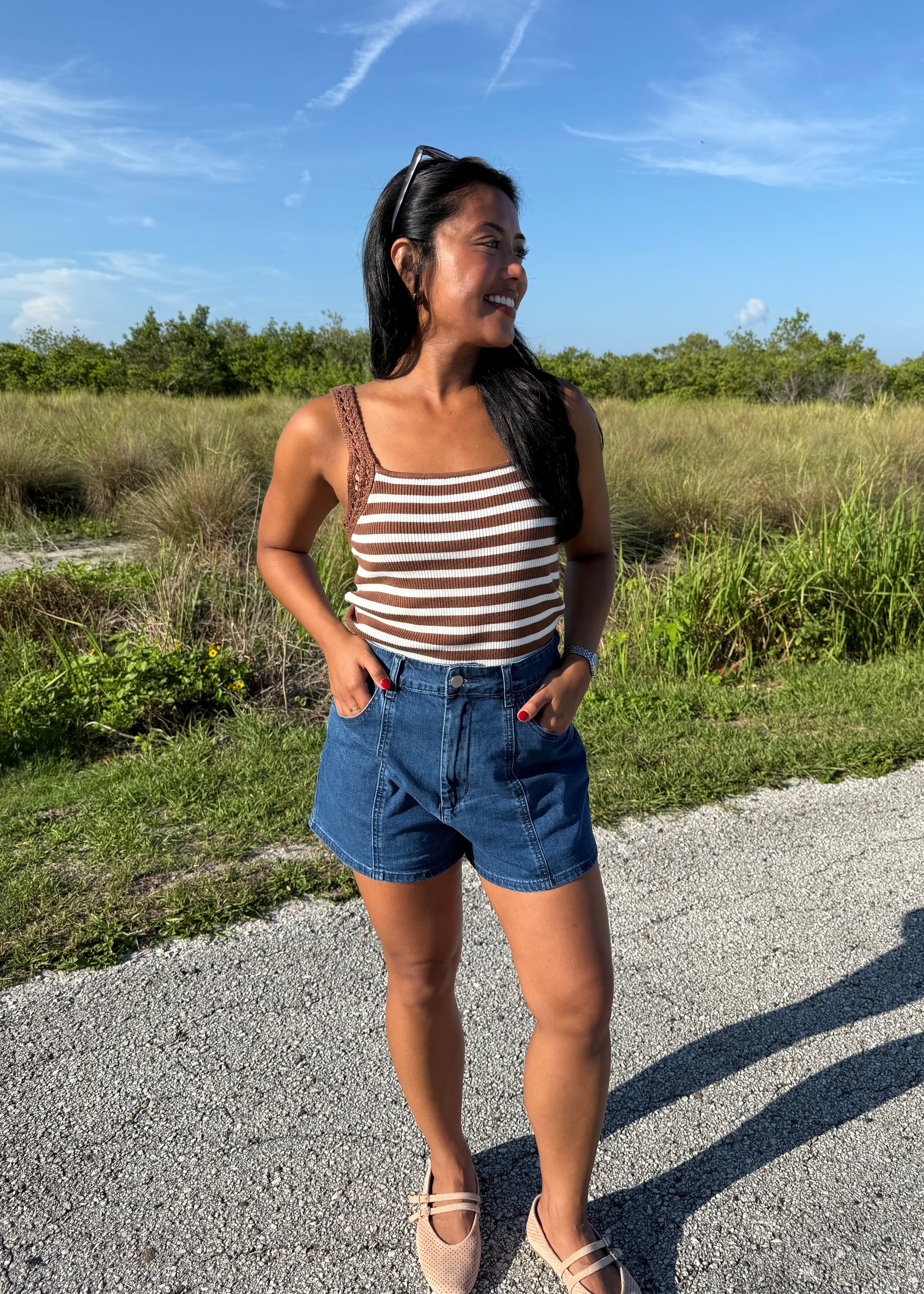 woman wearing denim shorts and a striped tank top on a grass background