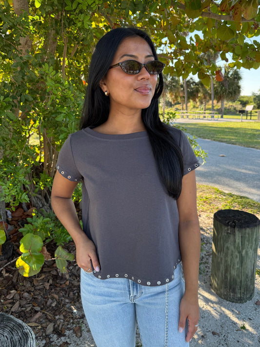 Woman wearing a gray top with decorative trim and light blue jeans outdoors.