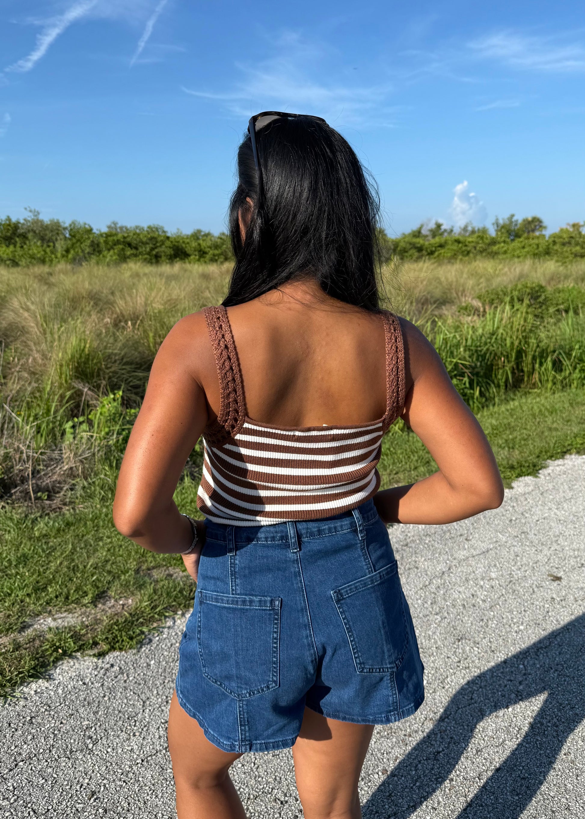 woman wearing a brown and white striped tank and jean shorts on a grass background