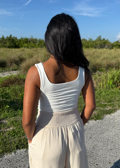 Woman wearing a white tank top and cream pants on a grass background
