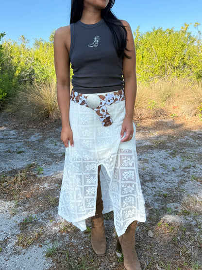 Person wearing a black tank top and white lace skirt with a patterned belt outdoors.