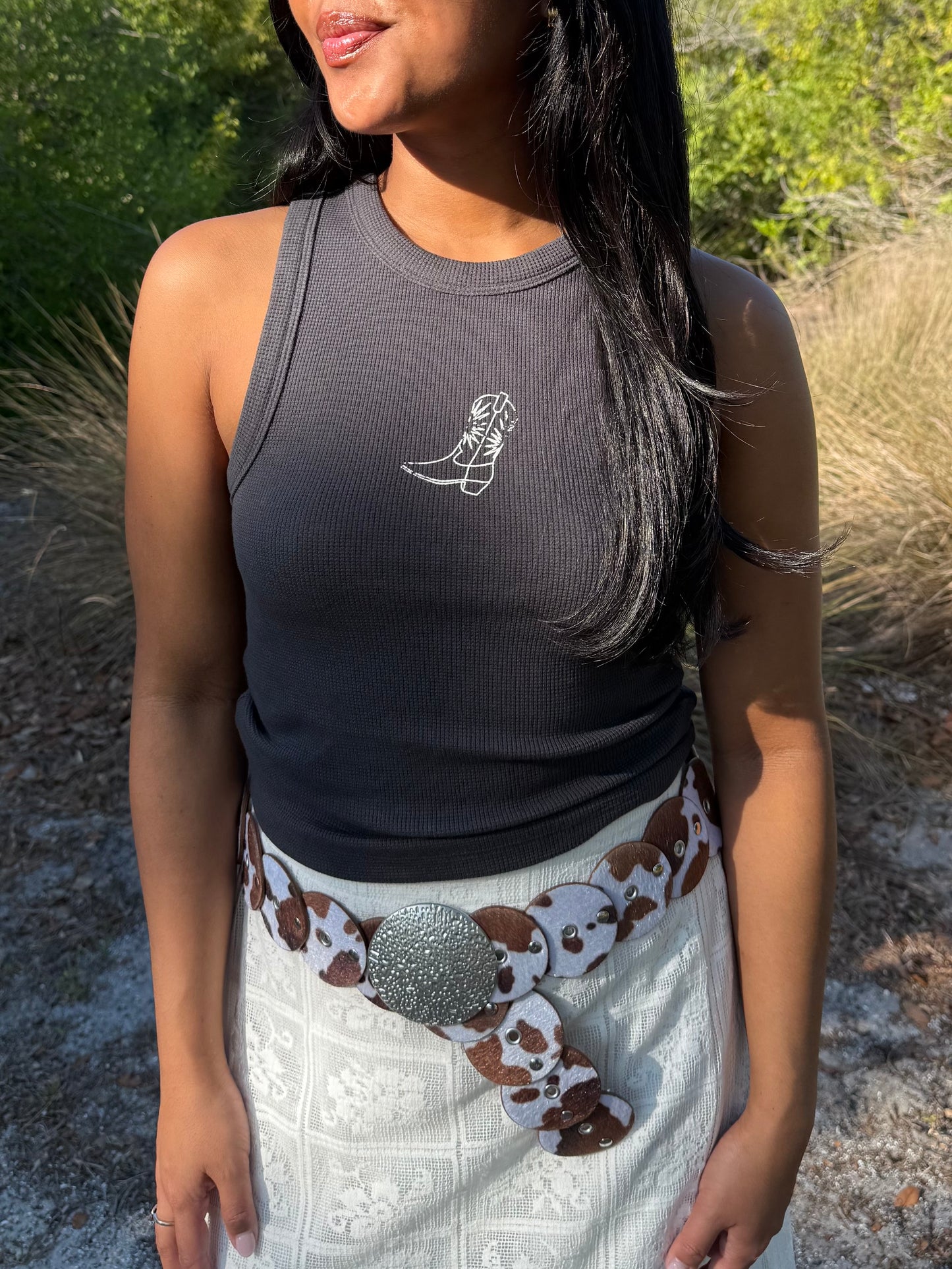 Woman wearing a dark gray tank top with a white boot design outdoors.