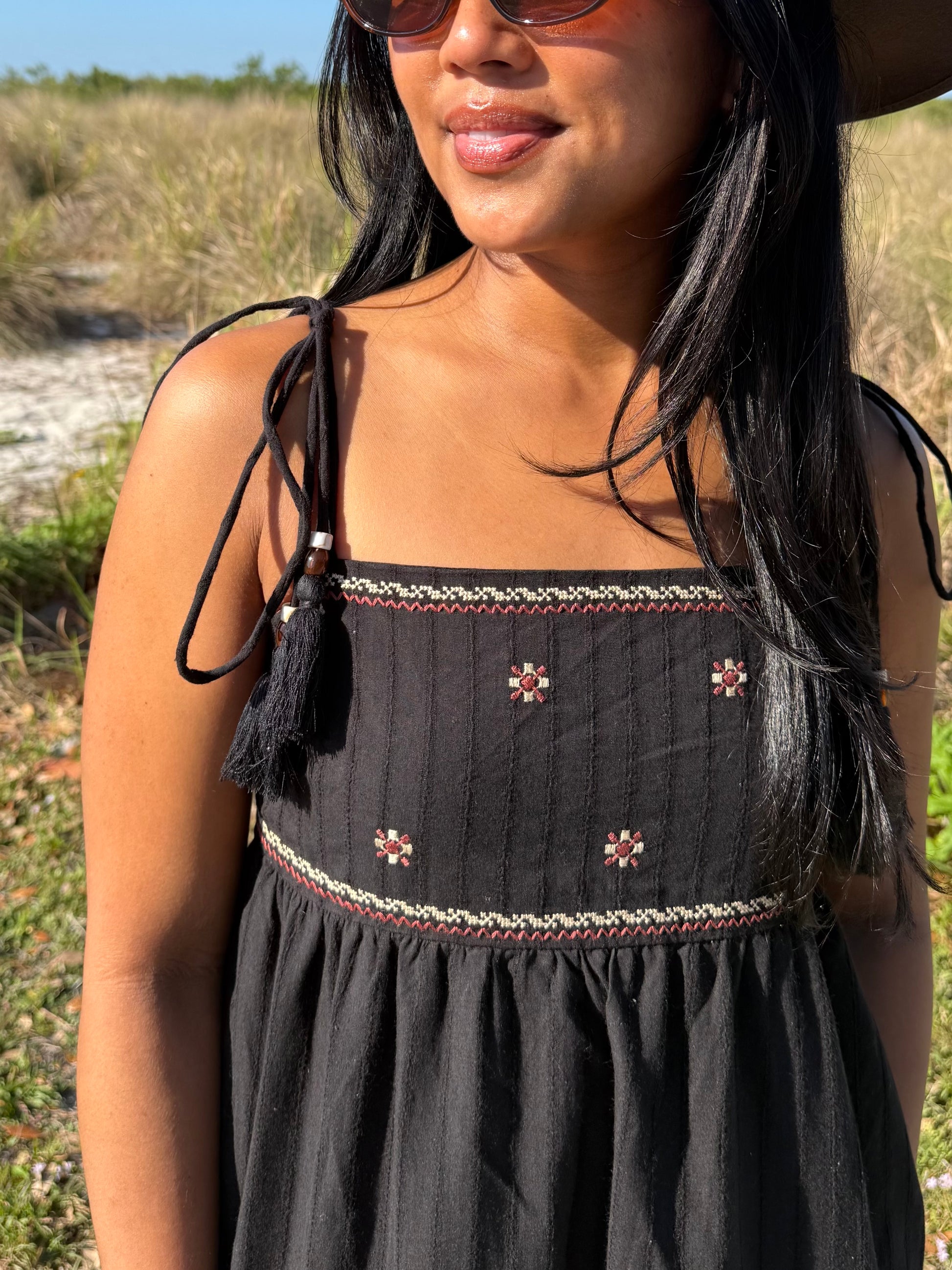 Woman wearing a black dress with floral embroidery in an outdoor setting