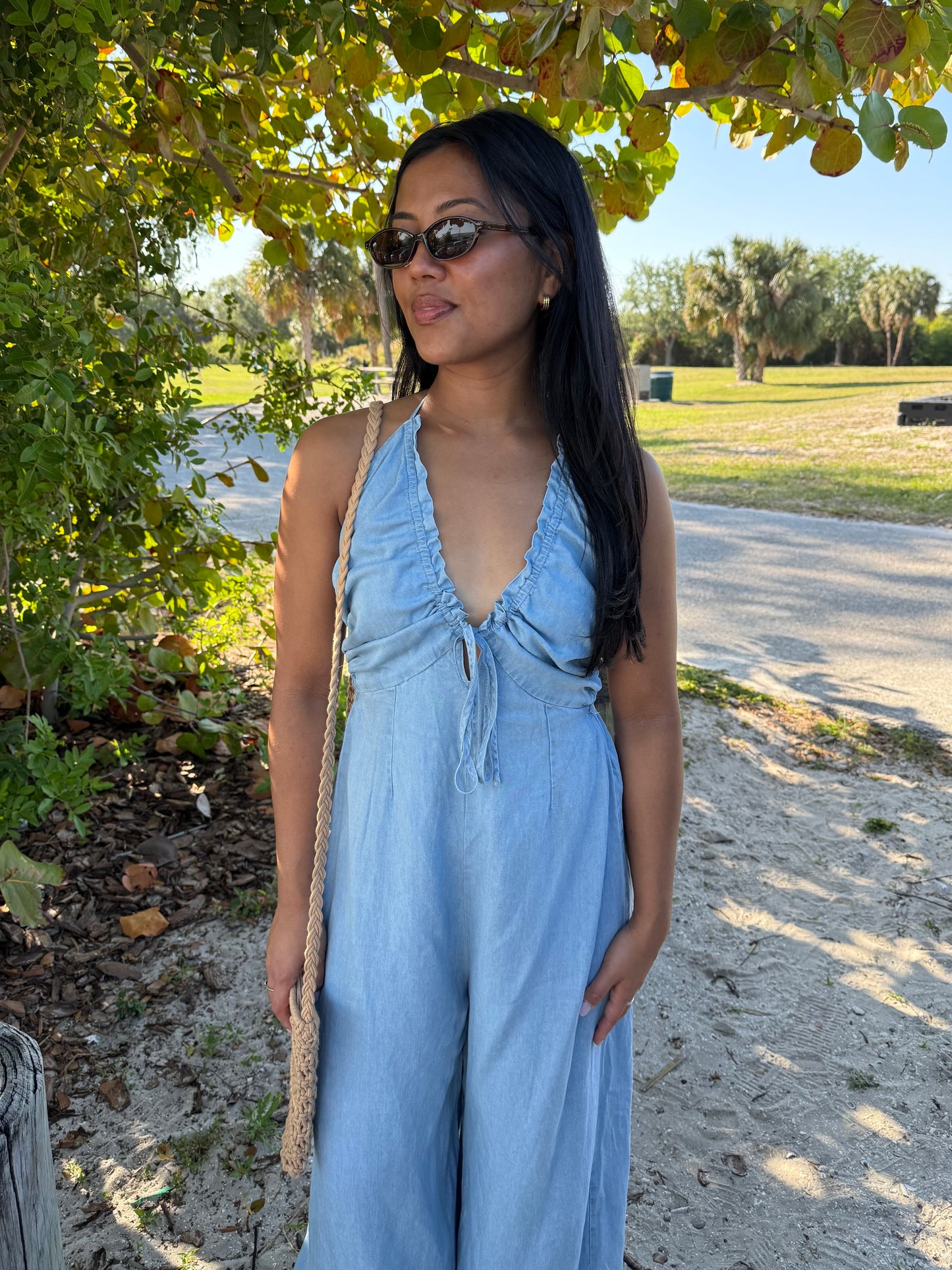 Woman in a blue jumpsuit standing outdoors under a tree