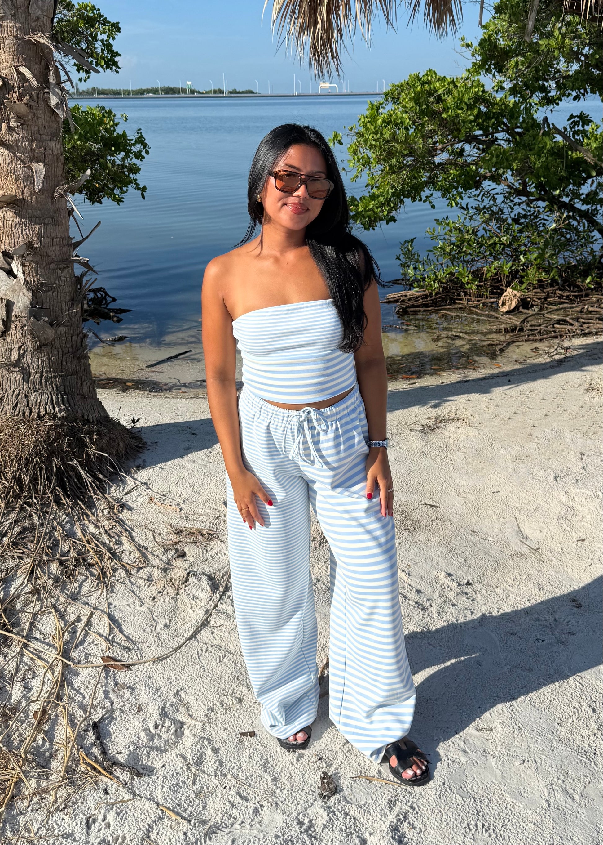 woman wearing striped top and striped pants on sand and water background