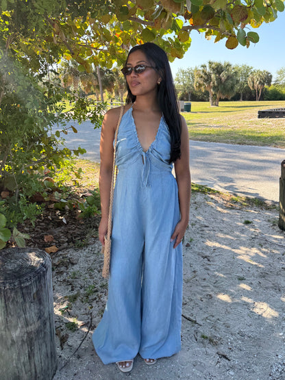 Woman in a blue jumpsuit standing outdoors under a tree