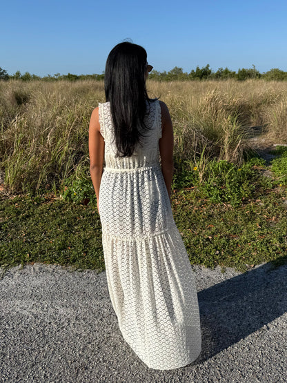 Woman in a white crochet dress standing in a field with a clear blue sky.