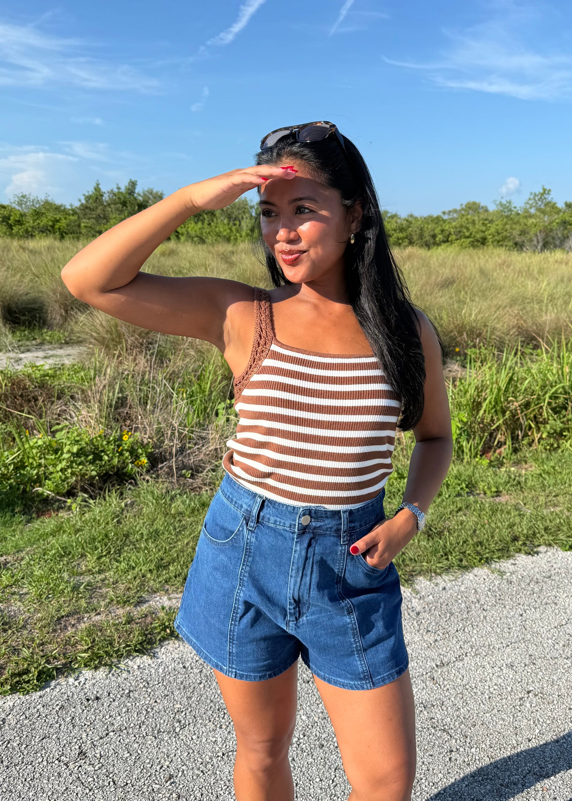 woman wearing a brown and white striped tank and jean shorts on a grass background