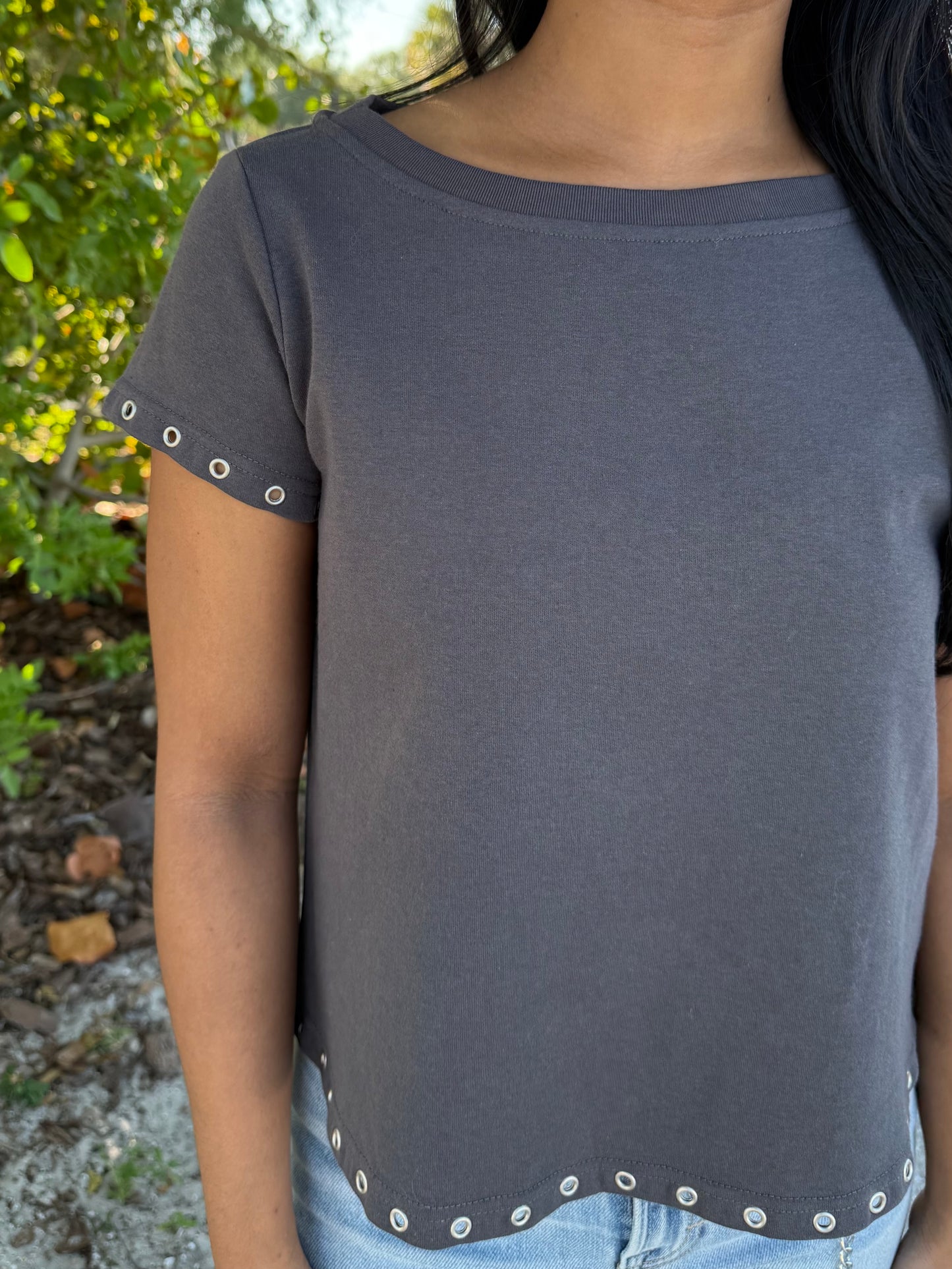 Person wearing a gray t-shirt with decorative trim outdoors