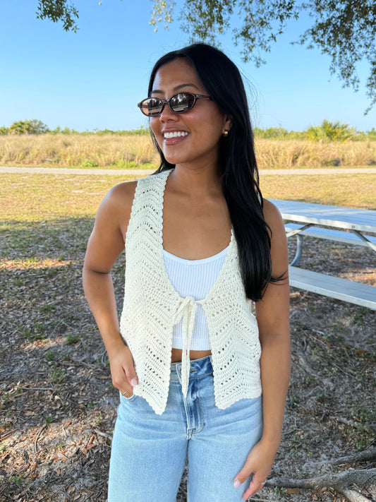 Woman wearing a white crochet vest over a light blue top and jeans, standing outdoors.