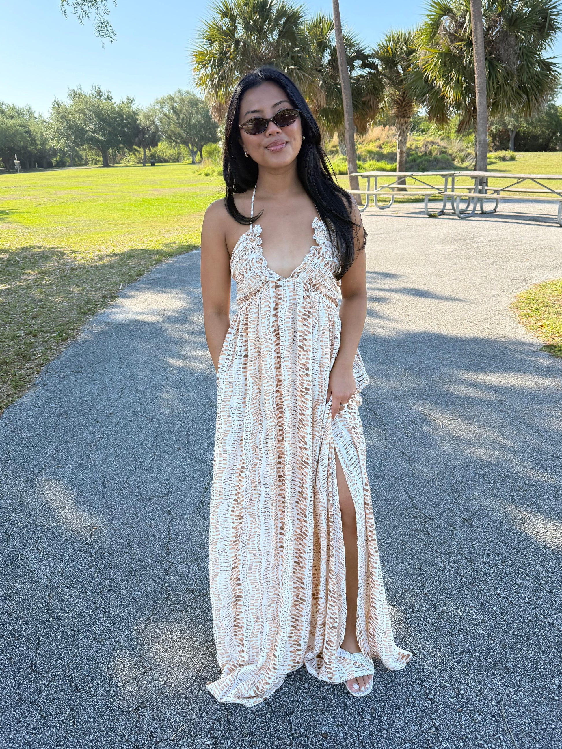 Woman in a printed white dress standing on a path with greenery in the background