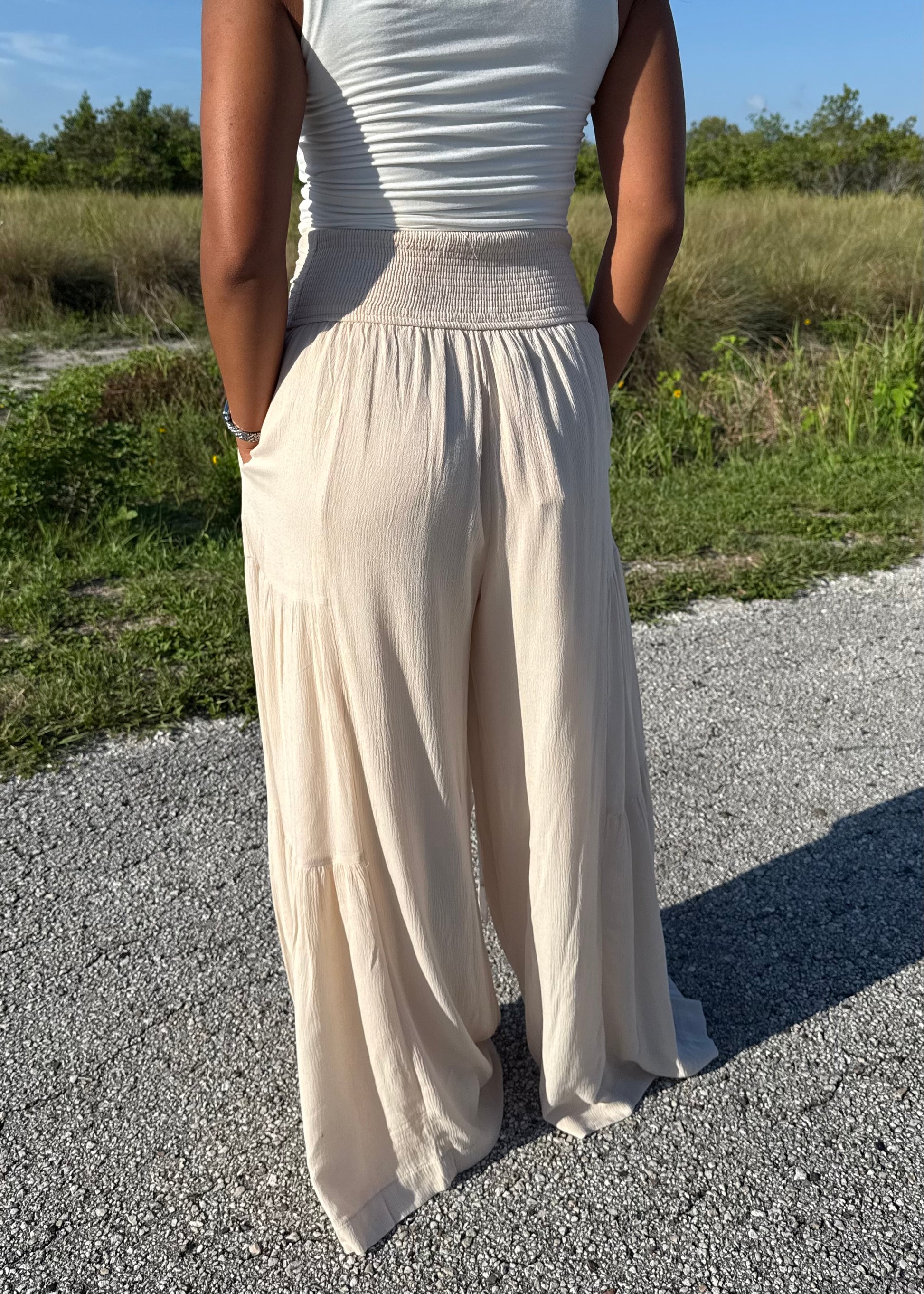 Woman wearing a white tank and shell colored pants on a grass background
