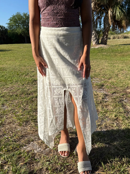 Person wearing a white lace skirt with a brown top in a grassy outdoor setting