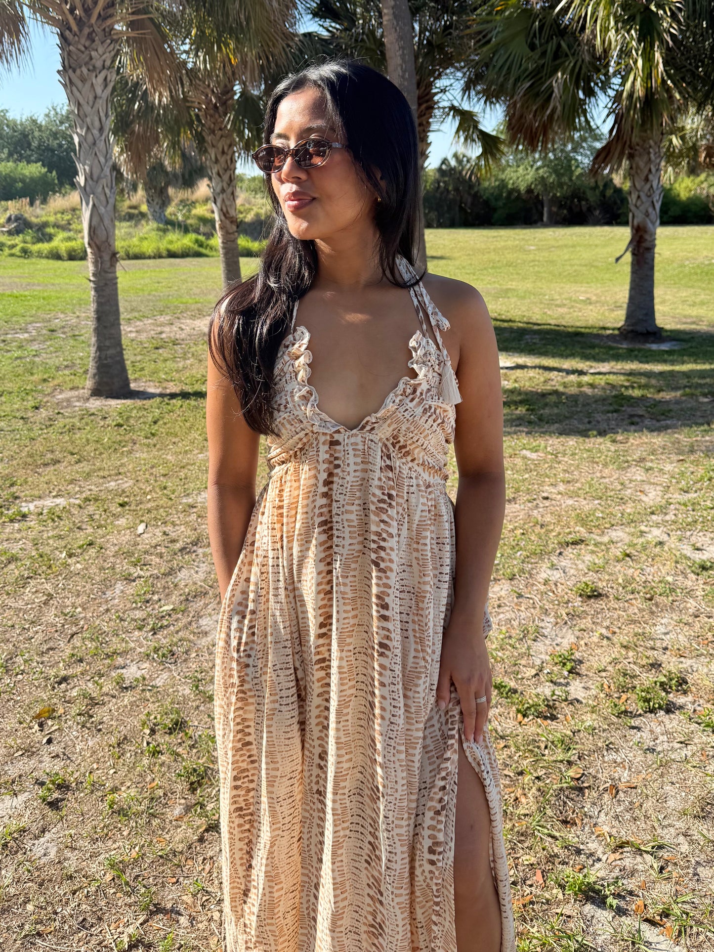 Woman in a patterned dress standing in a grassy area with trees.
