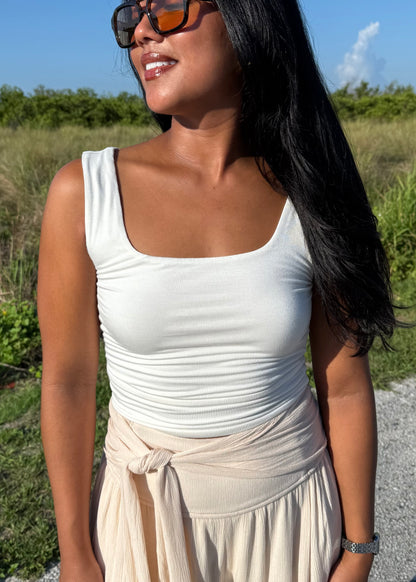 Woman wearing a white tank top and cream pants on a grass background