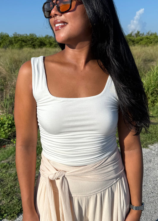 Woman wearing a white tank top and cream pants on a grass background