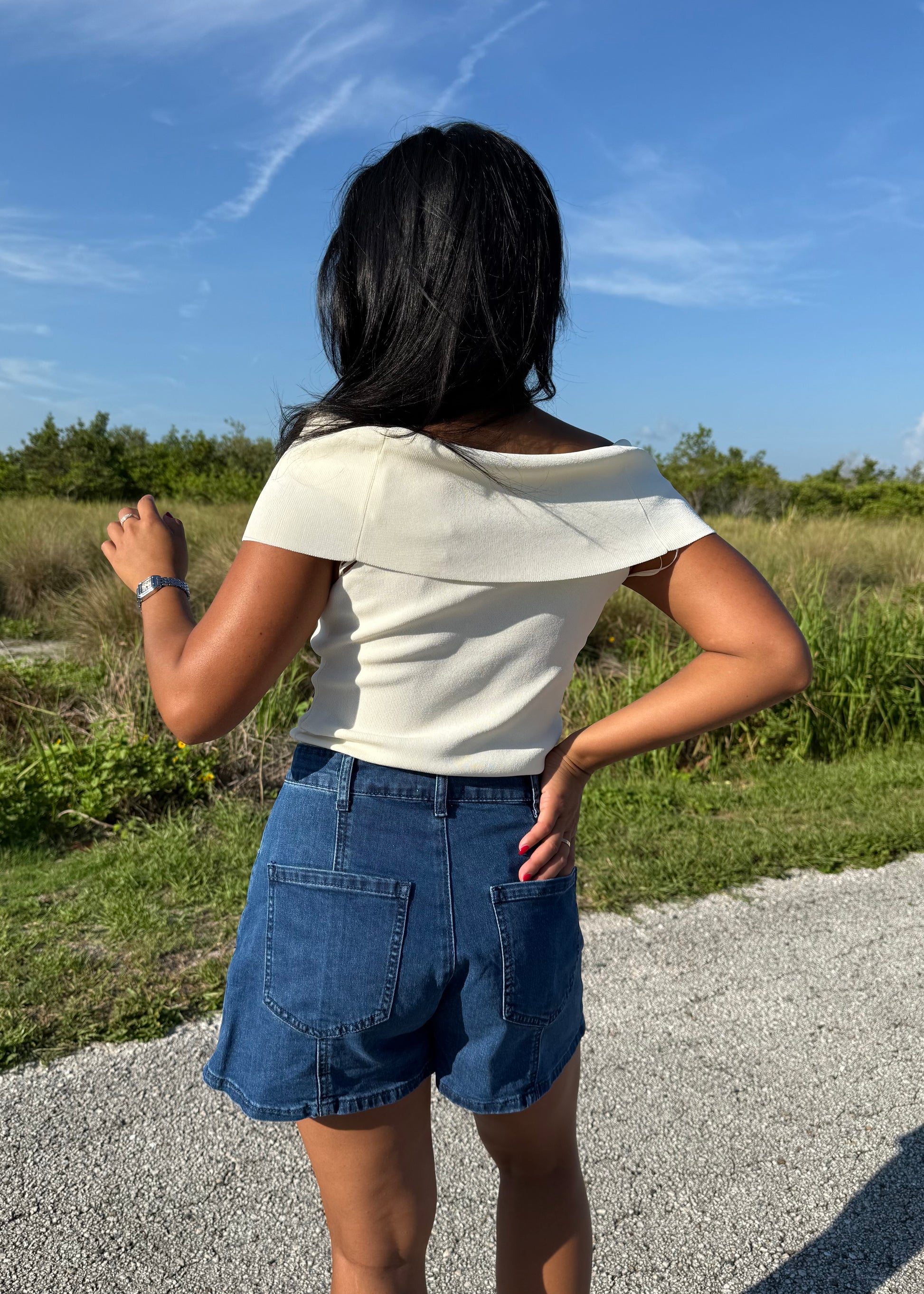 woman wearing a white top and denim shorts on a grass background