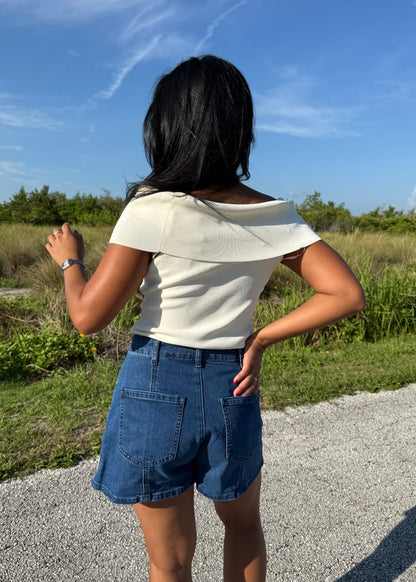 woman wearing a white top and denim shorts on a grass background