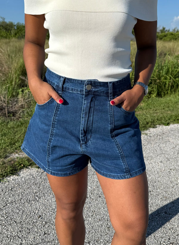 woman wearing denim shorts and a white top on a grass background