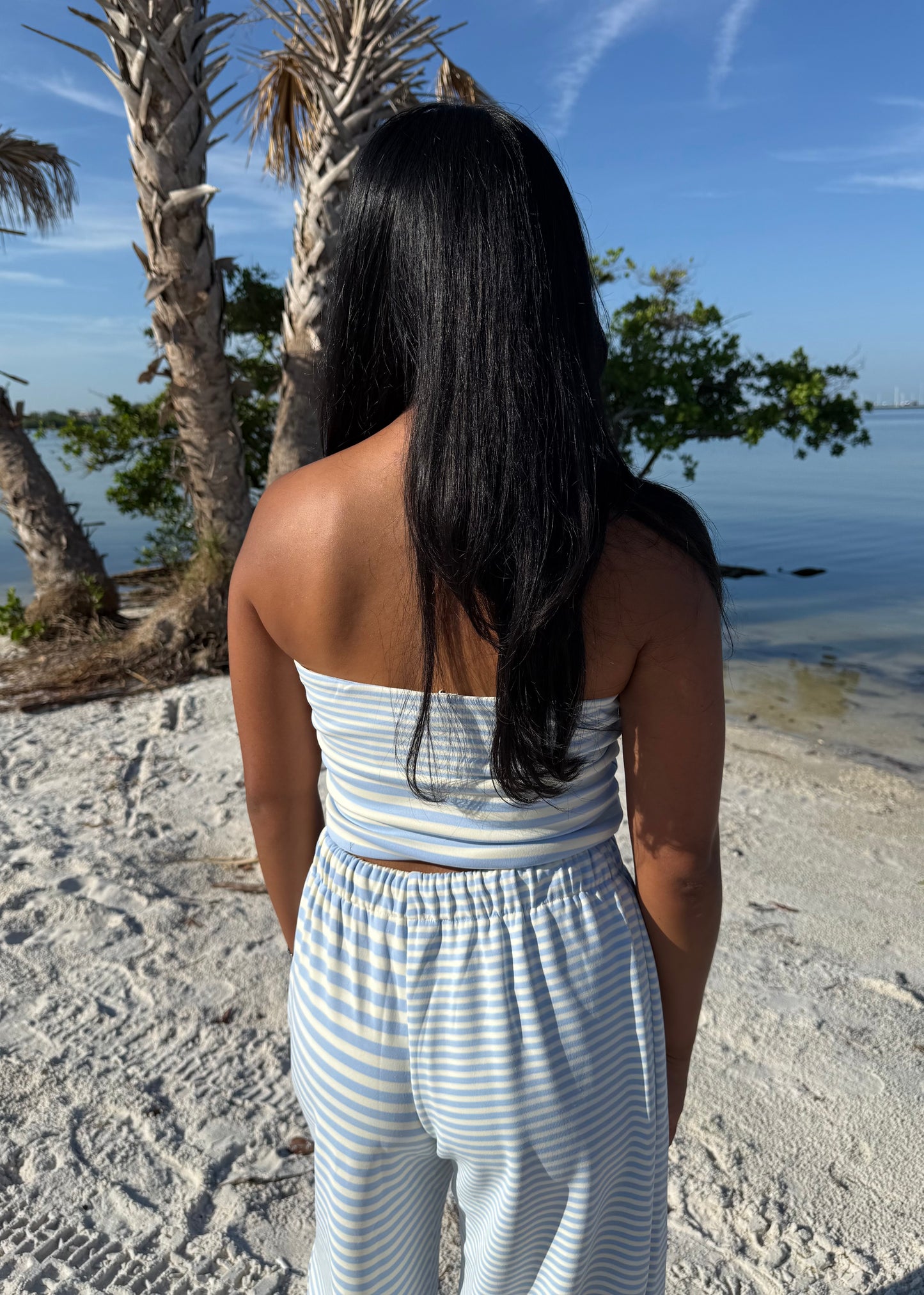 woman wearing striped top and striped pants on sand and water background