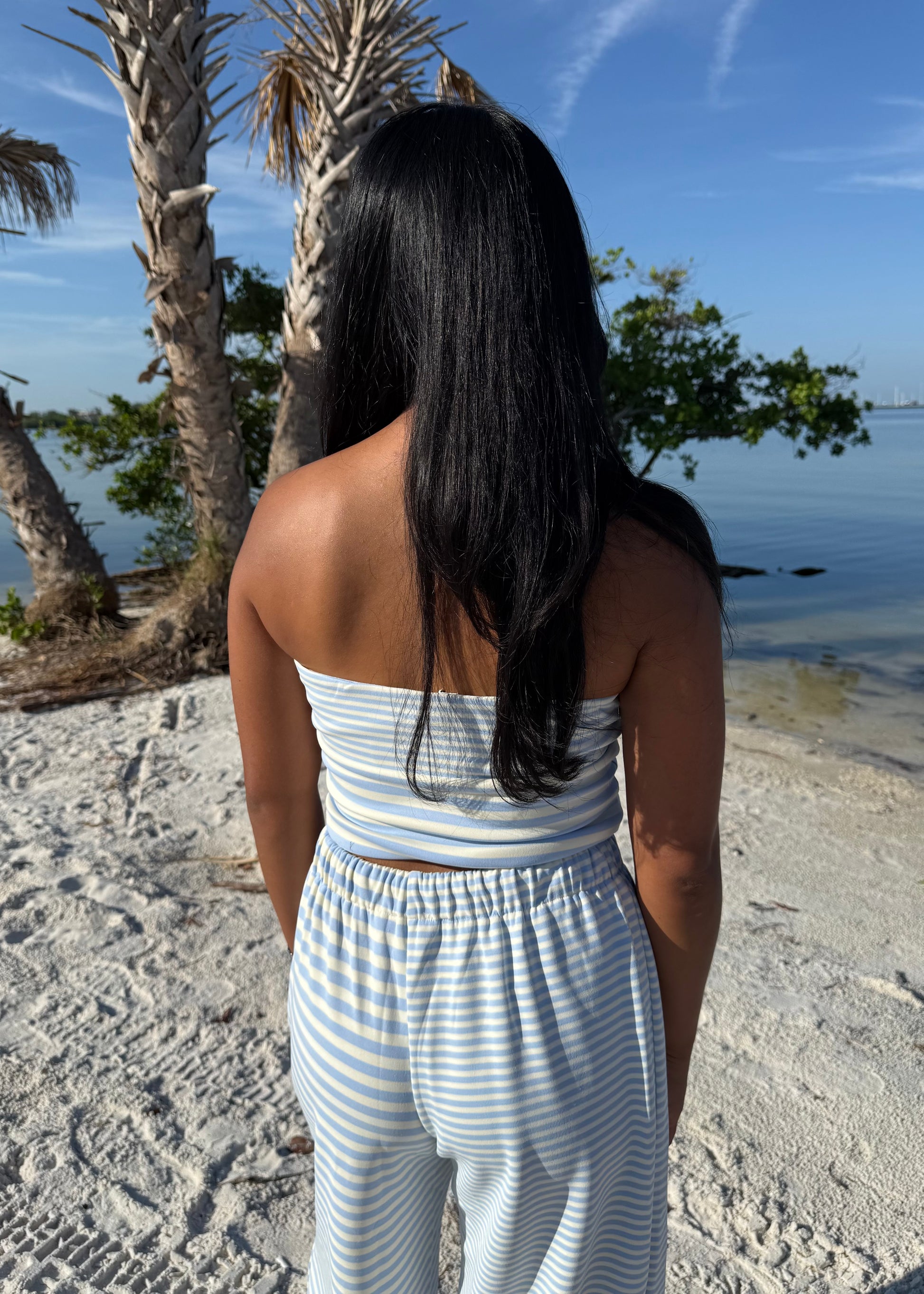woman wearing striped top and striped pants on sand and water background