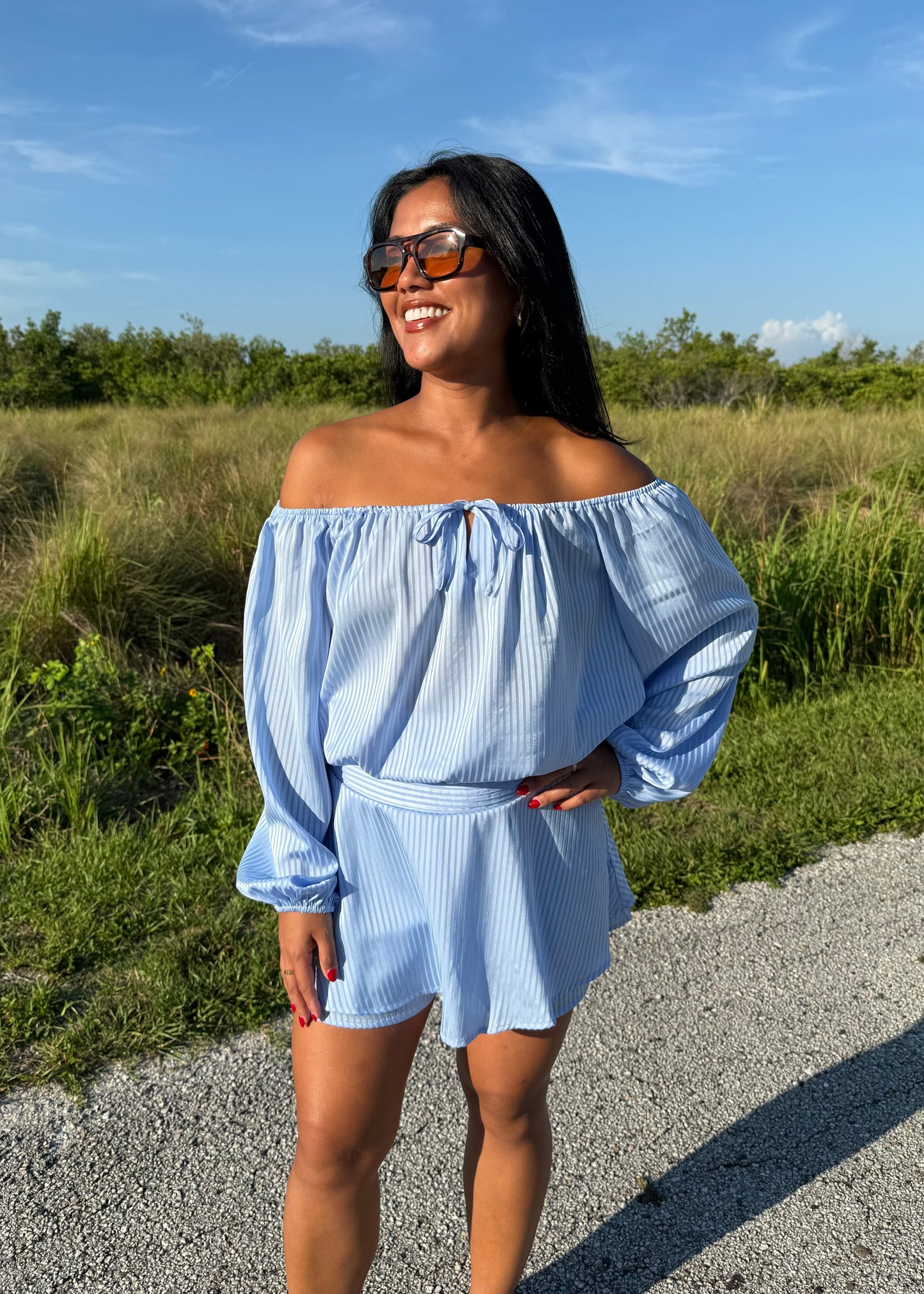 Girl wearing a blue off the shoulder long sleeve romper on a grass background