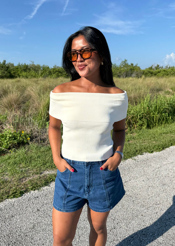 woman wearing a white top and denim shorts on a grass background