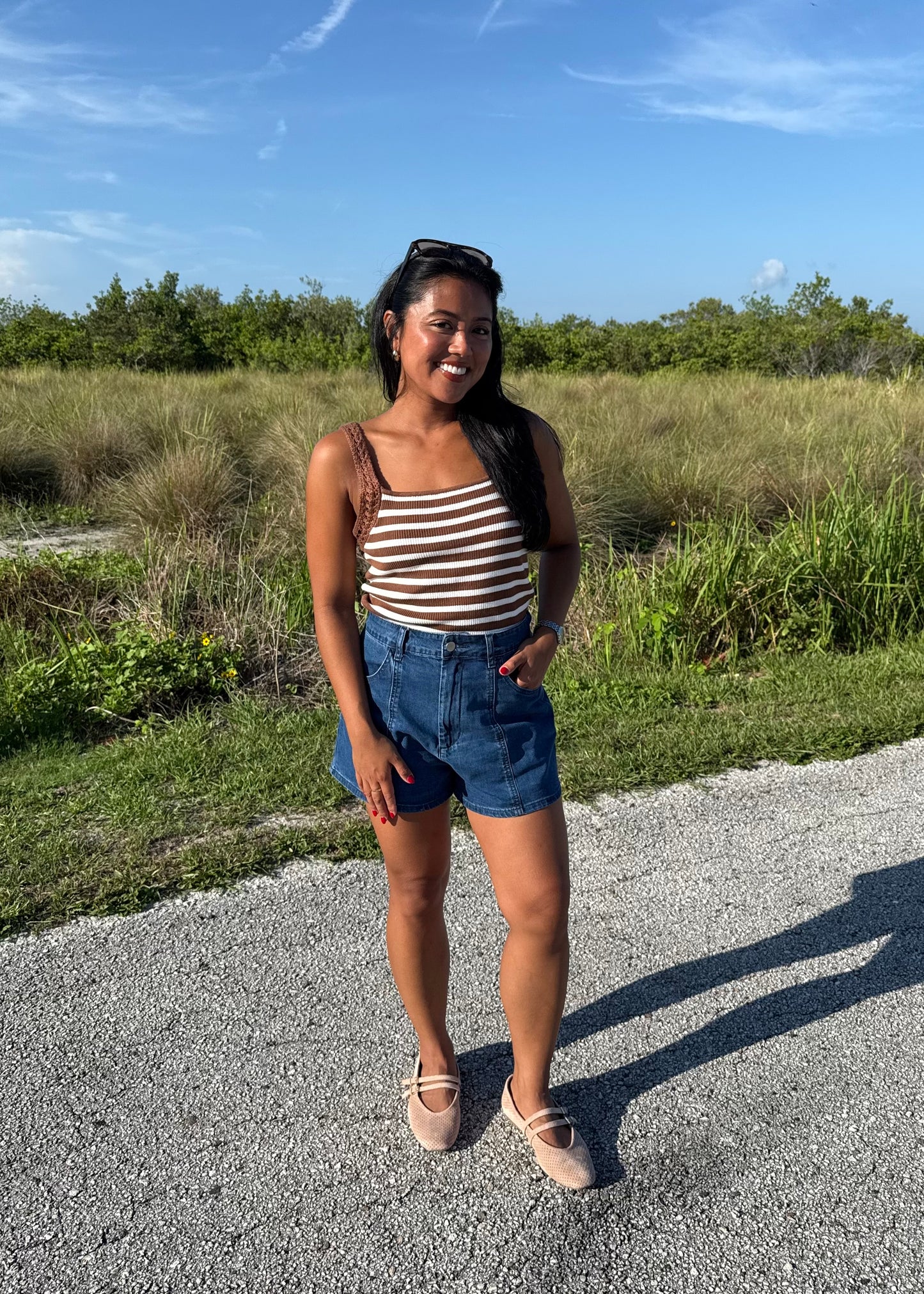 woman wearing a brown and white striped tank and jean shorts on a grass background