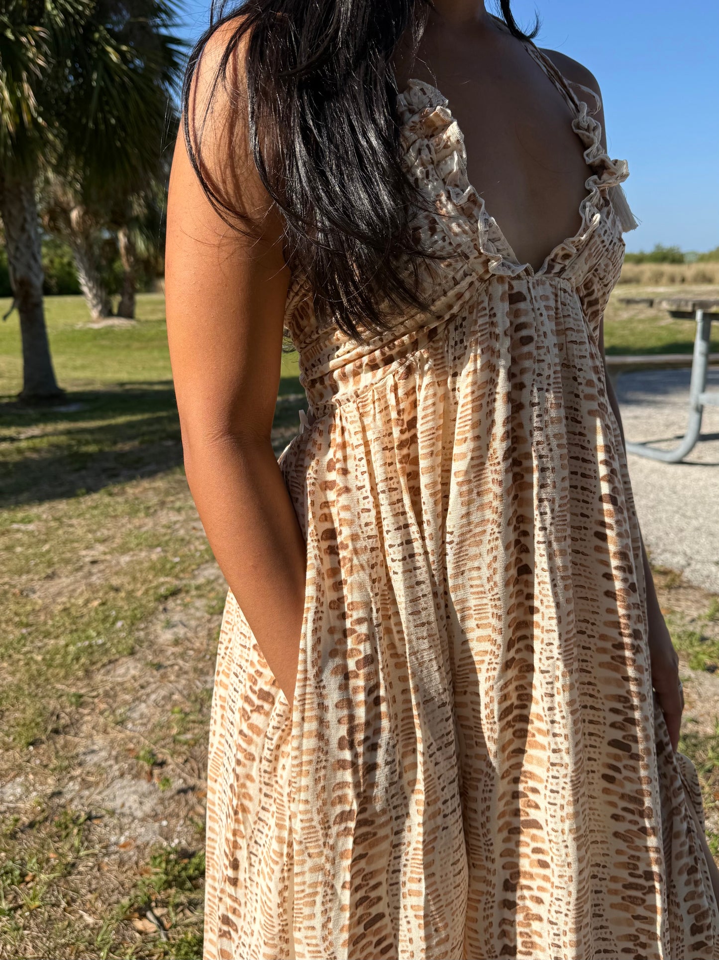 Woman wearing a patterned dress outdoors with trees and grass in the background