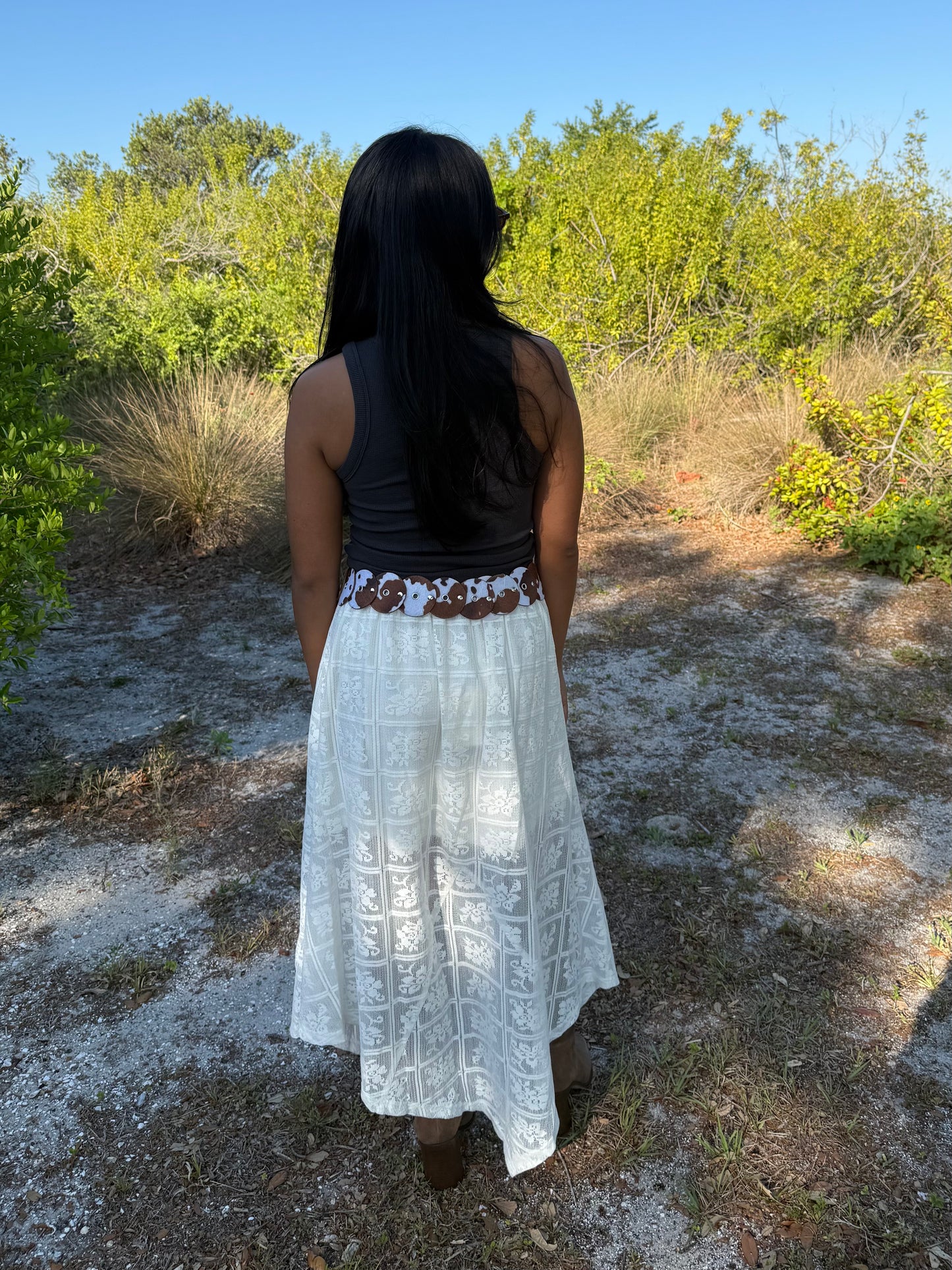 Person wearing a white dress with a patterned belt in a natural setting