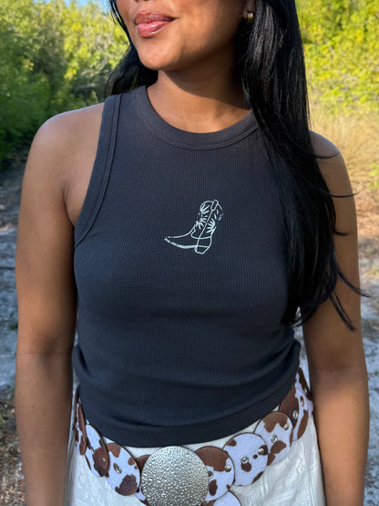 Woman wearing a black tank top with a white boot design outdoors