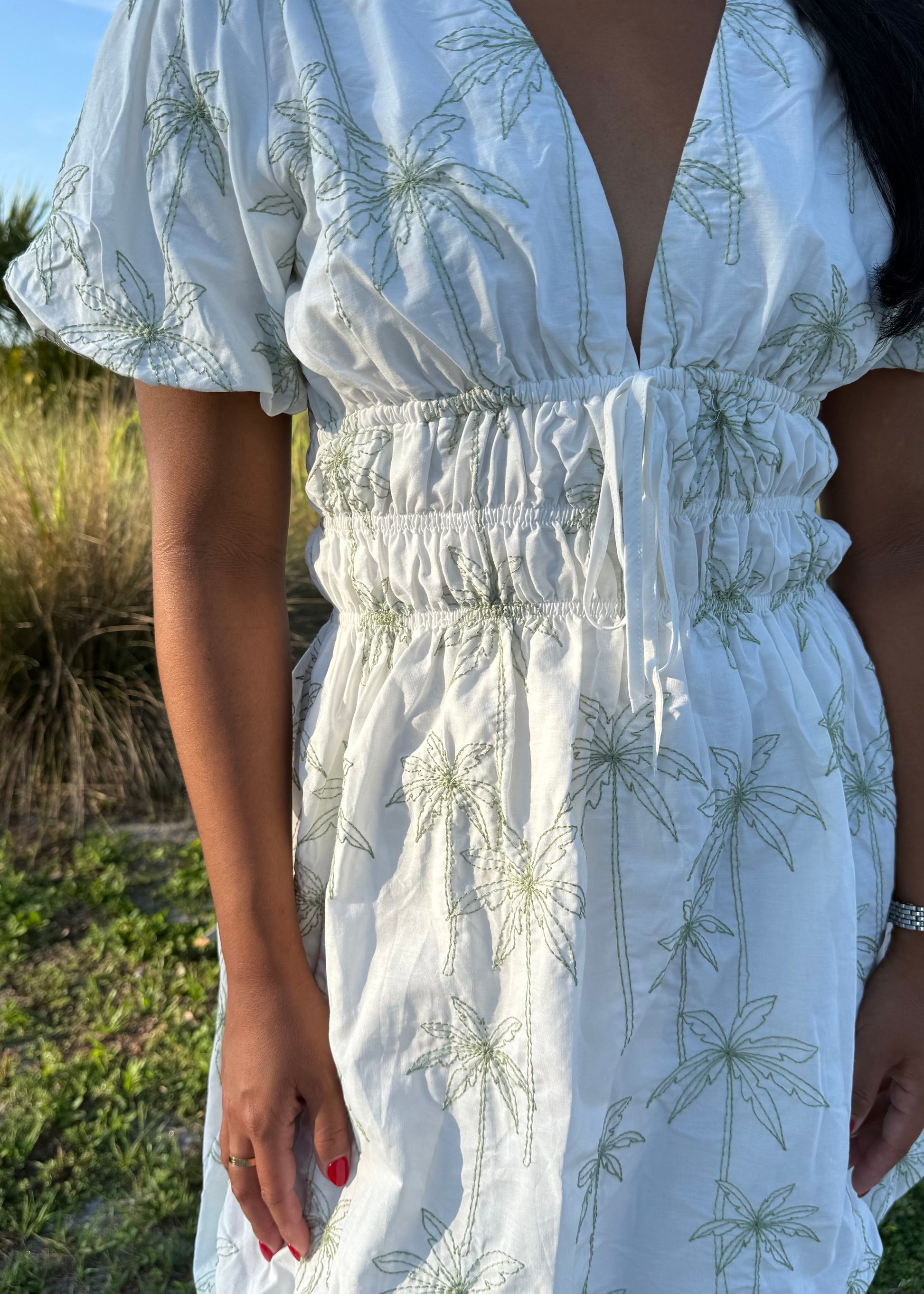 Girl wearing white mini dress with green palm tree print on a grass background.