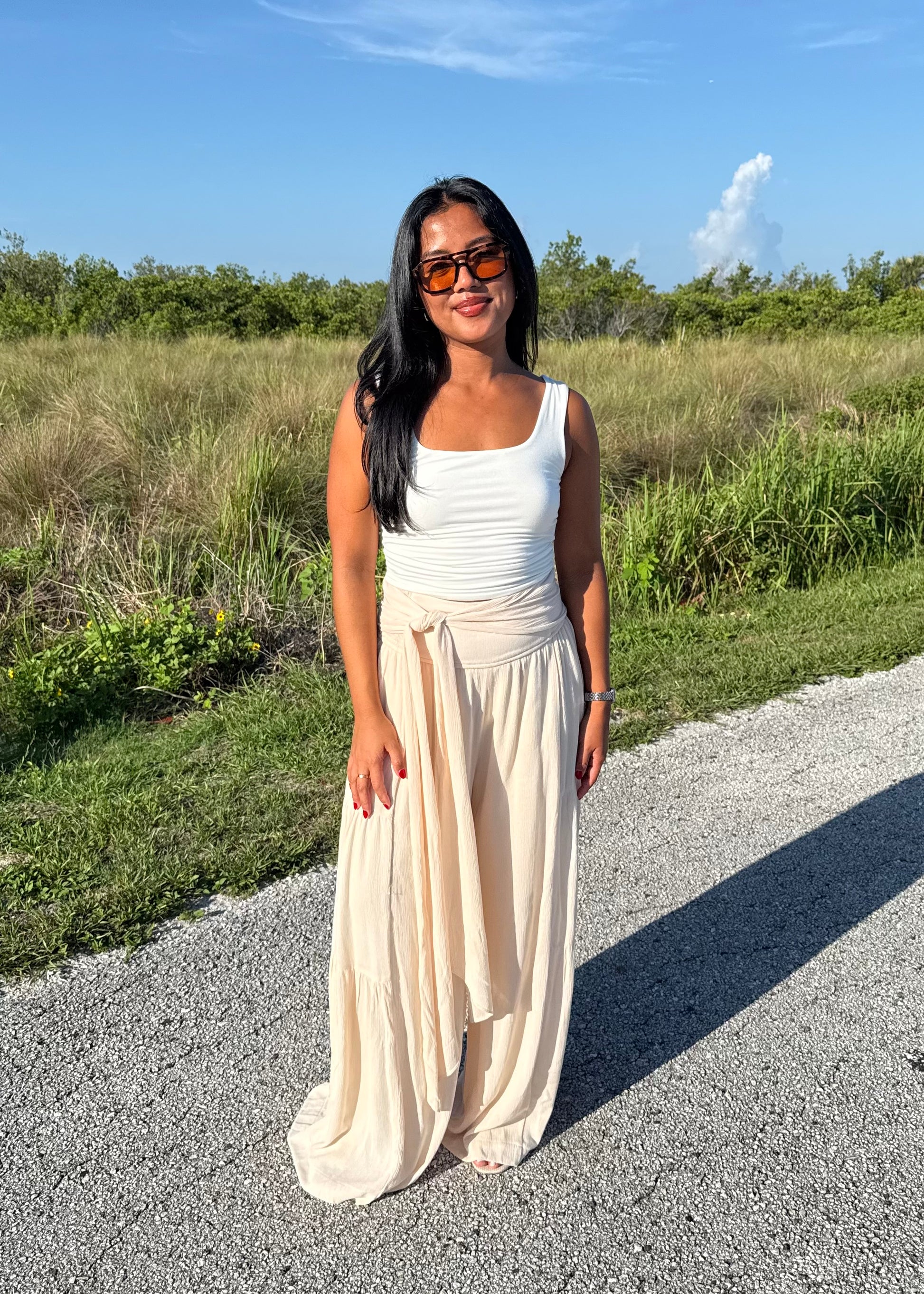 Woman wearing a white tank top and cream pants on a grass background
