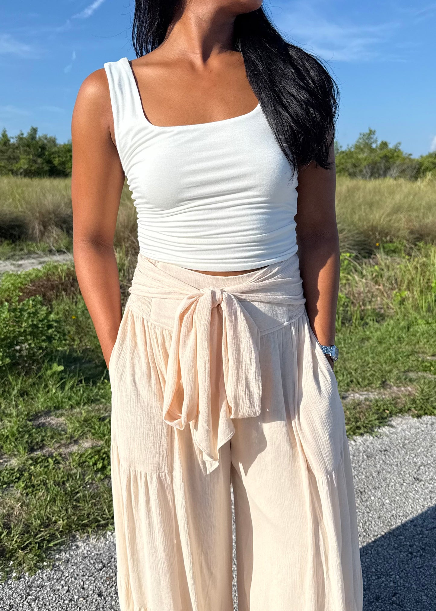 Woman wearing a white tank and shell colored pants on a grass background