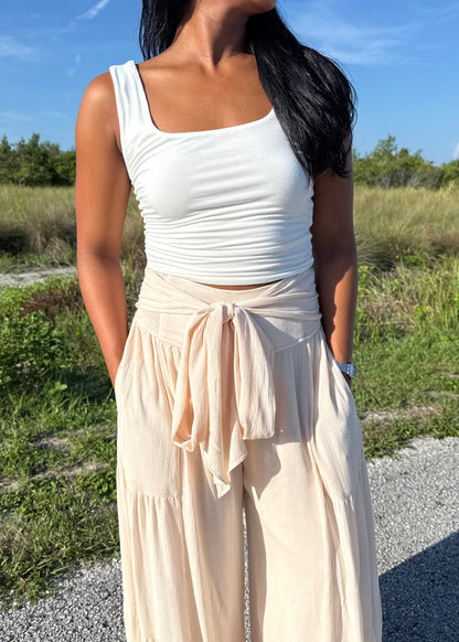 Woman wearing a white tank and shell colored pants on a grass background