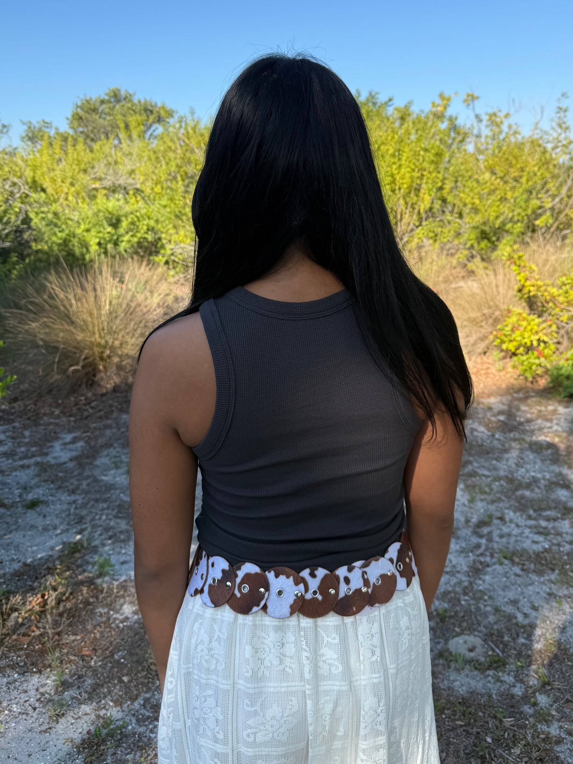 Person wearing a dark tank top and white skirt with a patterned waistband in a natural setting.