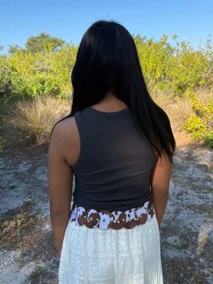 Person wearing a dark tank top and white skirt with a patterned waistband in a natural setting.