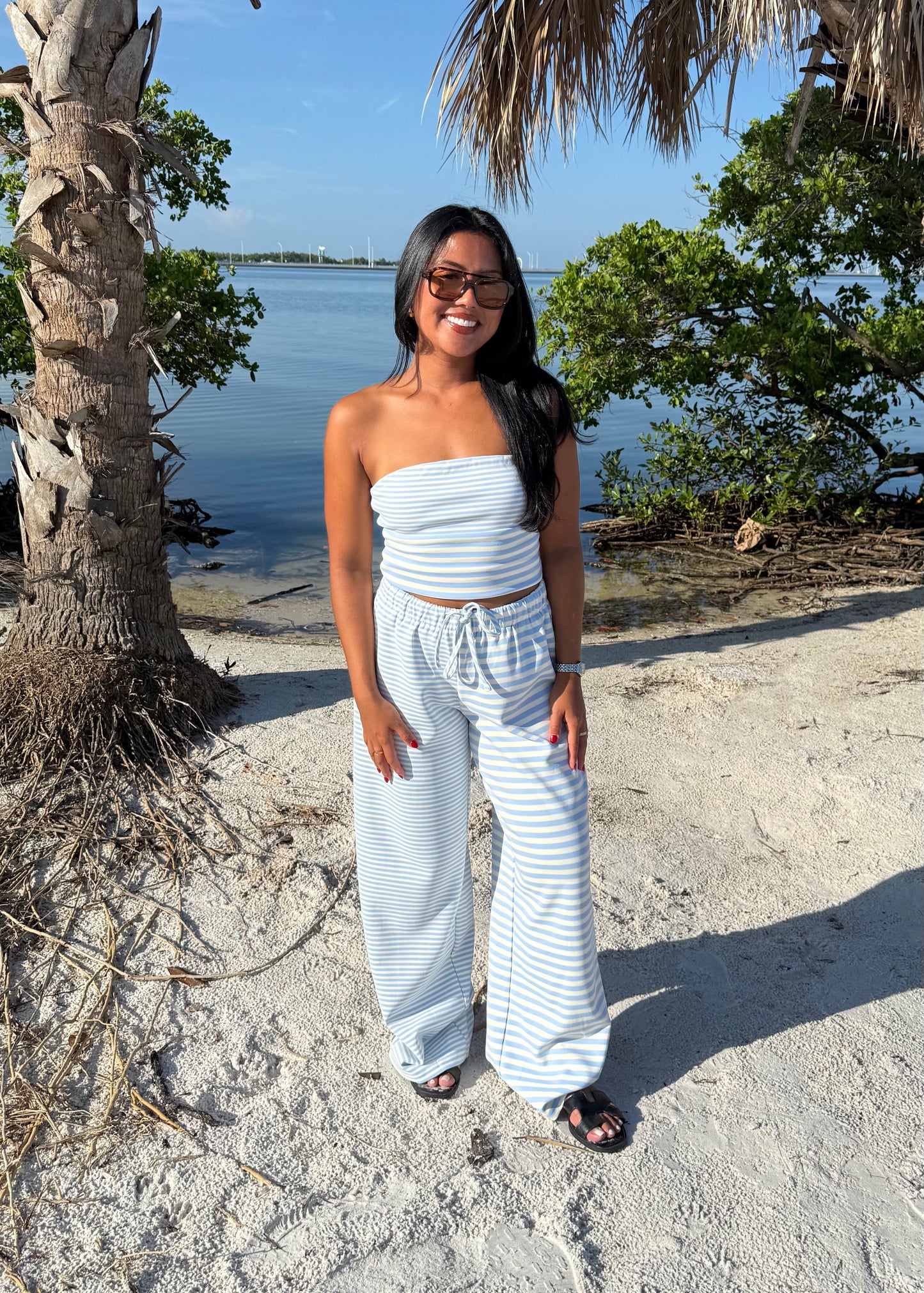 woman wearing striped top and striped pants on sand and water background