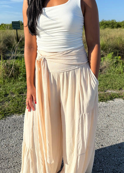 Woman wearing a white tank and shell colored pants on a grass background