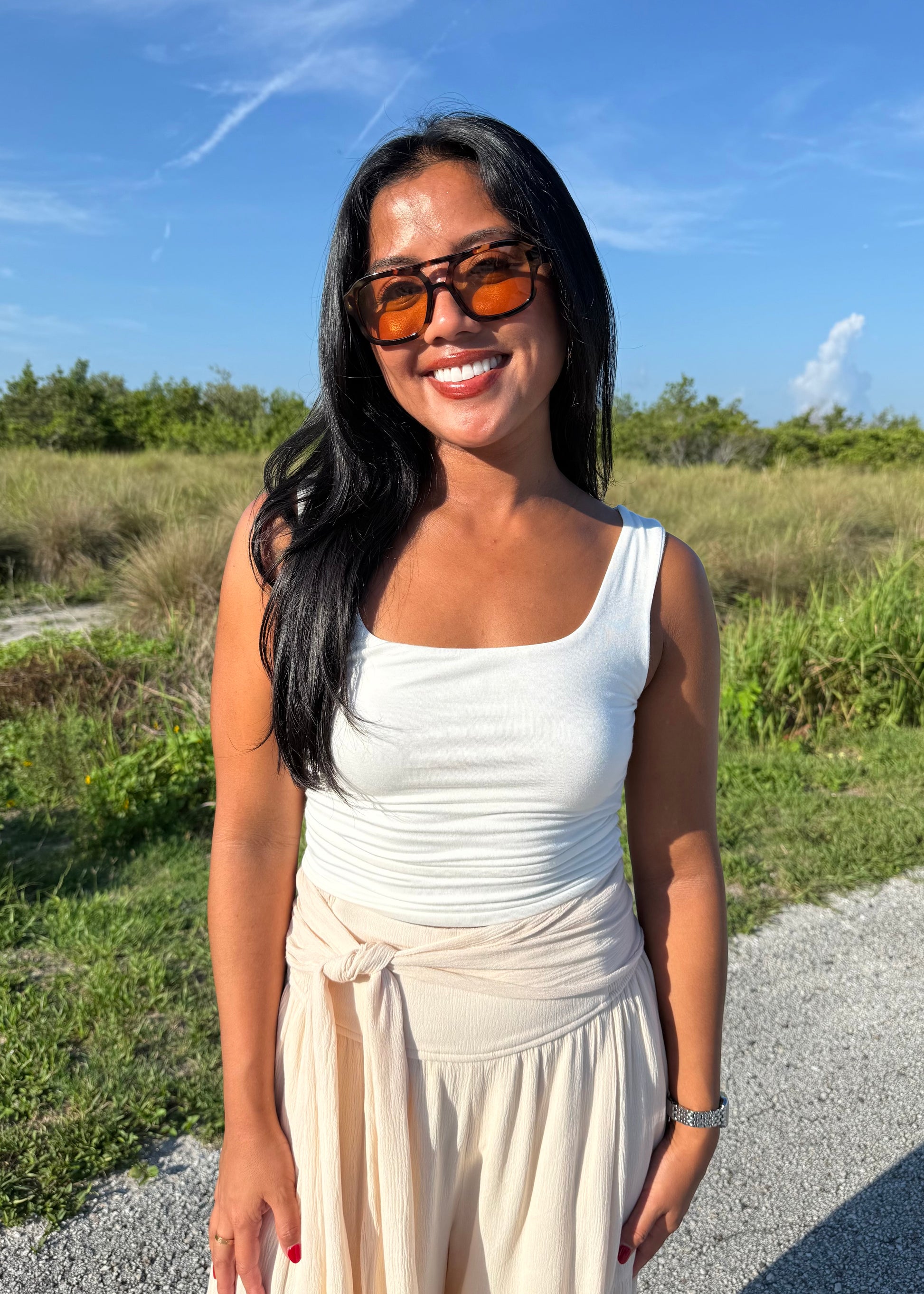 Woman wearing a white tank top and cream pants on a grass background